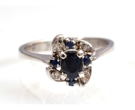 A sapphire and diamond ring, an oval cut sapphire within a scroll frame of round brilliant cut diamonds and round cut sapphir