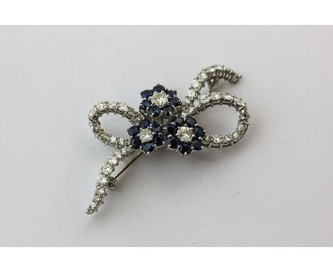 A sapphire and diamond brooch in the form of three flower heads in a diamond set ribbon bow