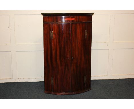 A George III mahogany bow front hanging corner cupboard with twin doors enclosing four shelves and two small drawers, 74cm