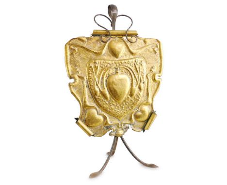 An Art Nouveau brass fire-screen, of shield shaped form embossed with hearts and tendrils on a beaten ground with rolled top 