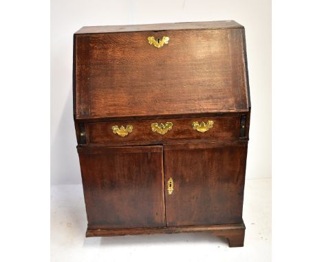 A Georgian oak bureau with fall front above frieze drawer flanked by slides and twin cupboard doors enclosing later fitted in