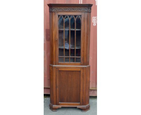 A late 19th century mahogany free standing corner cabinet with blind fret detail to the top section above single glazed door,