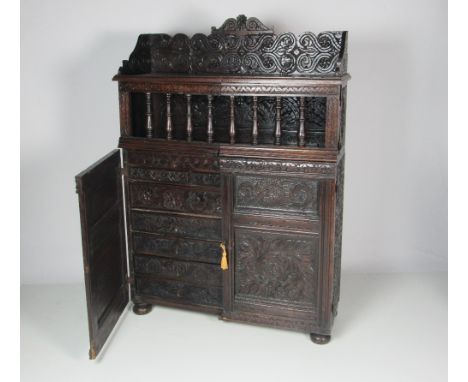 An unusual carved and blackened oak Cupboard, in the late 17th Century style, with carved back rail over two gate type doors,