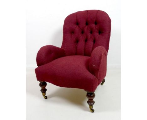 A Edwardian deep button back nursing chair upholstered with a burgundy fabric, raised on turned front legs and castors, 66 by