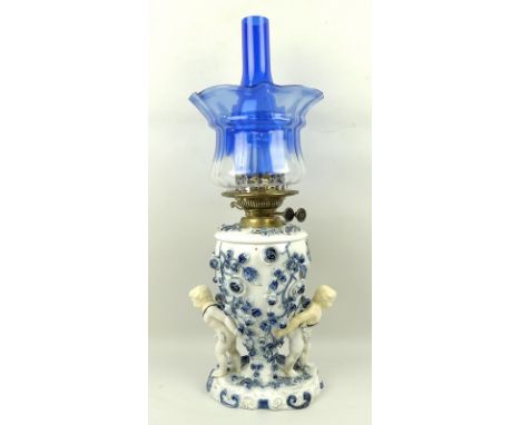 A Dresden blue and white paraffin lamp, circa 1890, the china base decorated with raised roses and a pair of putti supporting