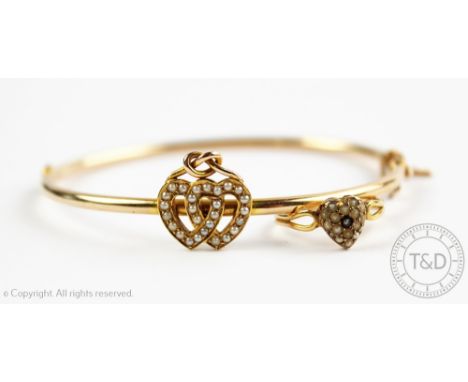 A Victorian bangle, the hinged rounded bangle set with entwined hearts with split seed pearls and surmounted by a Staffordshi
