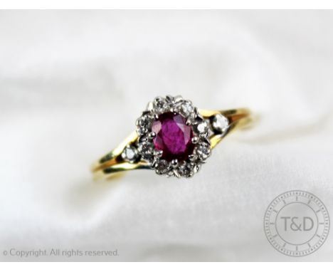 A ruby and diamond cluster ring, designed as a central ruby within a diamond set surround and further diamond set shoulders, 