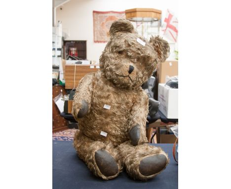 A large straw filled teddy bear, with original glass eyes and faux leather paws 