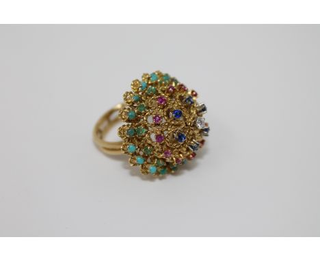 A high carat gold multi-gemstone ring, set with tiers of turquoise, emeralds, rubies, sapphires around a central brilliant cu