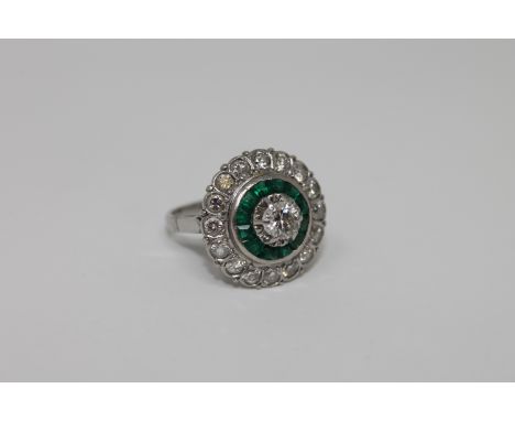 An emerald and diamond cluster ring, the principal brilliant cut stone surrounded by borders of calibre-cut emeralds and bril