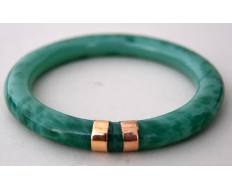 A Chinese mottled green jade and yellow metal mounted bangle of simple circular form, early 20th century, 6cmD