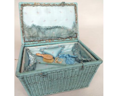 A beautiful vintage baby's layette basket containing an assortment of clothing and bedding. A pale blue wicker basket on smal
