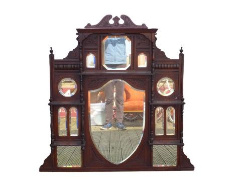 A Victorian mahogany overmantle mirror with central shield shaped bevelled glass, galleried above with shelf and with two she