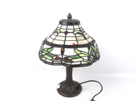 A Tiffany style table lamp. The metal stand modelled as a tree trunk, the leaded glass shade with green details, H34cm