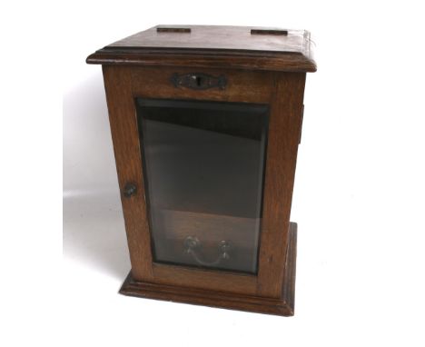 An early 20th century oak smokers cabinet. With a hinged cover, glazed door and single drawer below, containing a single pipe