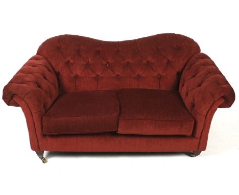 A contemporary two seater button back sofa. Upholstered in red fabric, raised on tapered supports, on casters, H88cm W174cm x