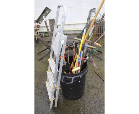 An assortment of garden tools. Including a saw, rake, spade, pickaxe, foldable ladder, etc.