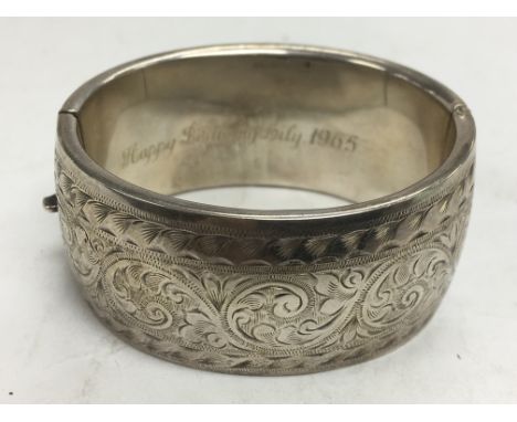 A silver bangle with engraved decoration.