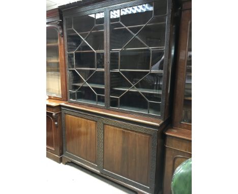 A Quality Edwardian Mahogany bookcase with blind fretwork, geometric glazed doors above a pair of cupboard doors with bracket