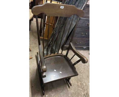 A modern stained wood high comb stick back rocking elbow chair, set on turned supports