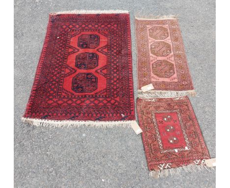 An Afghan handmade wool rug with red ground and navy decoration comprising three central motifs and a wide border - 1.6m x 1m