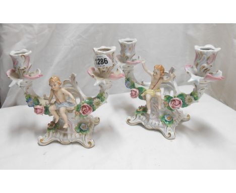 A pair of early 20th Century Sitzendorf porcelain figural candlesticks of rococo form, each decorated with a cavorting putti 