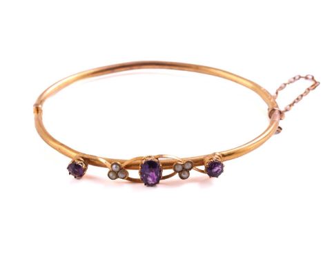 An Edwardian 9ct yellow gold bangle, mounted with an oval mixed cut amethyst flanked by three seed pearls and a round mixed c