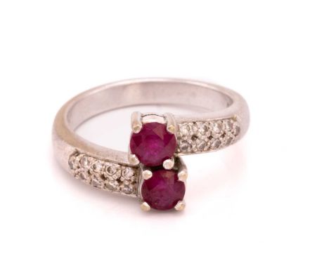 A ruby and diamond crossover ring, featuring two circular-cut rubies in claw setting, with pavé-set diamond shoulders to a D-