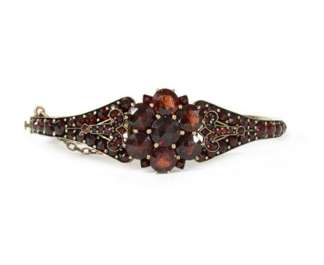 A late 19th century Bohemian garnet bangle, a central cluster claw set with rose cut garnets, with a fleur-de-lys at each sid