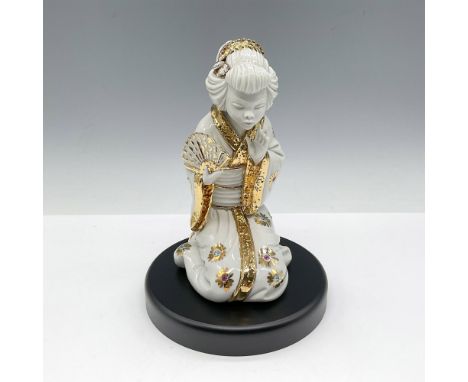 White porcelain kneeling figure, holding fan with gilt accents on black wooden base. Kimono is adorned with Swarovski colored