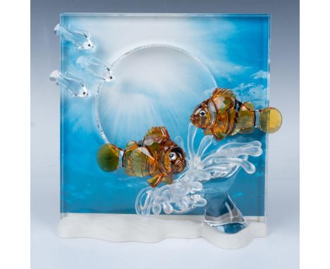 A beautiful pair of orange and black clownfish swim among a sea anemone, with a school of fish gracefully gliding above them 