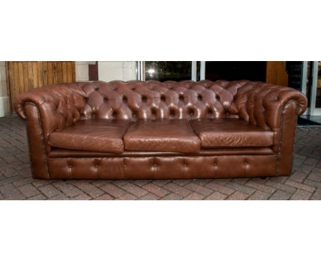 Brown Leather Three Seater Button Back Chesterfield Settee with three loose seat covers terminating on castor feet. 82'' in w