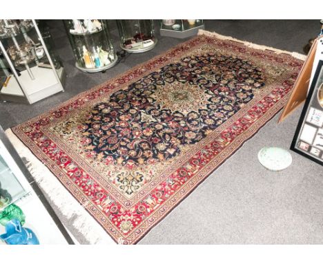 A Turkish Handmade Carpet In The Persian Style with a central Medallion blue ground with floral decoration and a ruby red bor