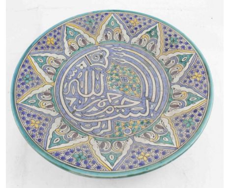 A large tin glazed earthenware Islamic ceramic charger decorated with nask script to a floral ground and stylised multi-borde