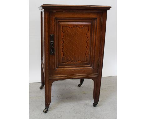 An Edward VII oak pot cupboard with single panel satin cross-banded door closing with a copper Arts &amp; Crafts handle, on s