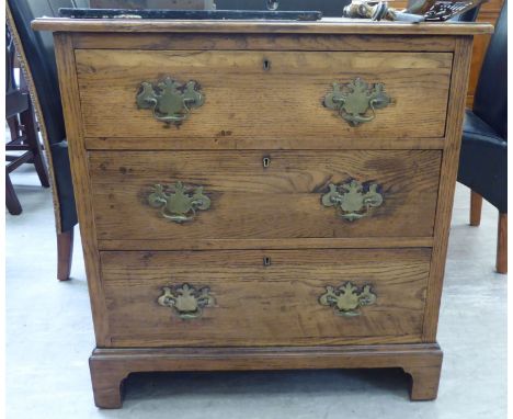An early 20thC light oak chest, the three graduated long drawers with cast brass bail handles, on shaped backplates, raised o