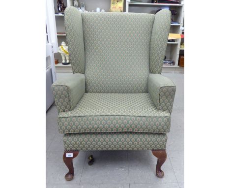 A mid 20thC wingback armchair, the fabric covered back, arms and seat raised on stubby cabriole forelegs        S