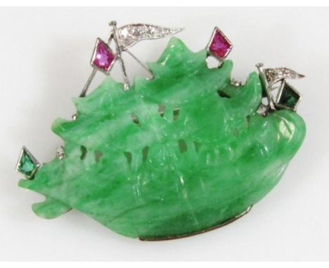 A 20thC green jade brooch, formed as a junk, partially pierced and set with purple and pink stones, on a white metal ground w