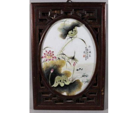 A Chinese porcelain plaque, of oval outline in a carved wooden surround, polychrome decorated with lilies in a pond setting, 