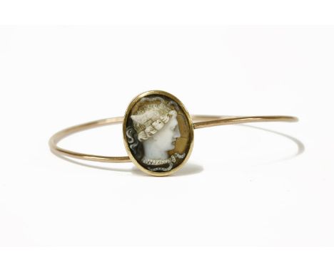 A gold carved hardstone cameo bangle, with an oval cameo depicting Medusa in white to a brown ground, a plain rub-over frame 