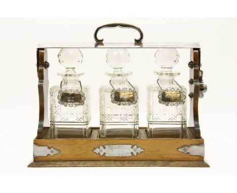 An early 20th century oak three bottle tantalus, containing three cut glass decanters with silver spirit labels, 37 cm x 15 c