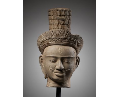 A SANDSTONE HEAD OF SHIVA, ANGKOR WAT STYLEKhmer Empire, 12th century. His face finely carved with full pursed lips, framed b