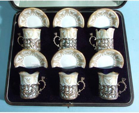 A set of six Royal Worcester coffee cans and saucers in pierced silver cup holders decorated with frolicking putti, dated Lon