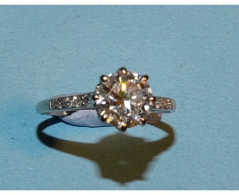 A solitaire diamond ring claw-set a brilliant-cut diamond of approximately 1ct between diamond-set shoulders, in unmarked whi