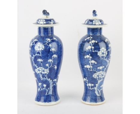 A pair of blue and white vases; each one with a domed cover and Dog of Fo finial. Both decorated with a typical design of pru