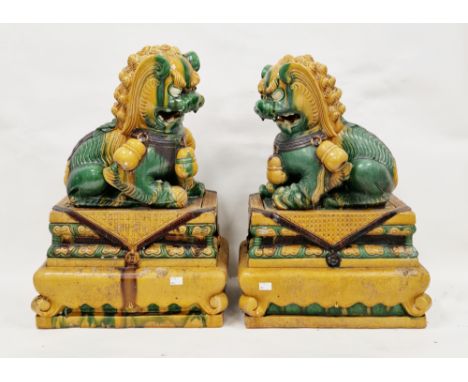 Pair of Chinese stoneware Sancai glazed buddhist lion dogs&nbsp;on bases, 20th century, each stylised dog modelled with a paw