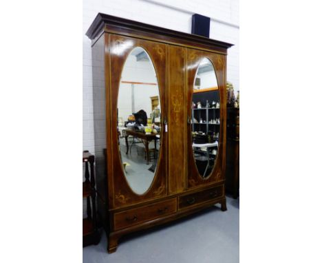A mahogany and inlaid wardrobe, the pediment top over a pair of oval bevelled mirrored doors with floral inlay above two long