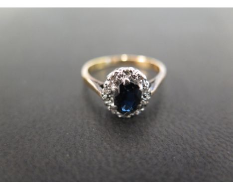 An 18 ct gold sapphire and diamond dress ring - the central oval sapphire surrounded by ten small round cut diamonds in a pla