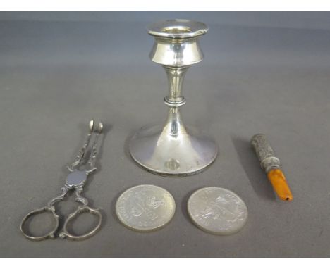 A silver hallmarked candlestick, two silver Birmingham Crowns, a silver cheroot holder and a pair of silver tongs 