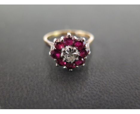 A 15 ct gold diamond and ruby cluster ring set with a central round cut diamond of approx. 0.3 to 0.35 cts - surrounded by ei